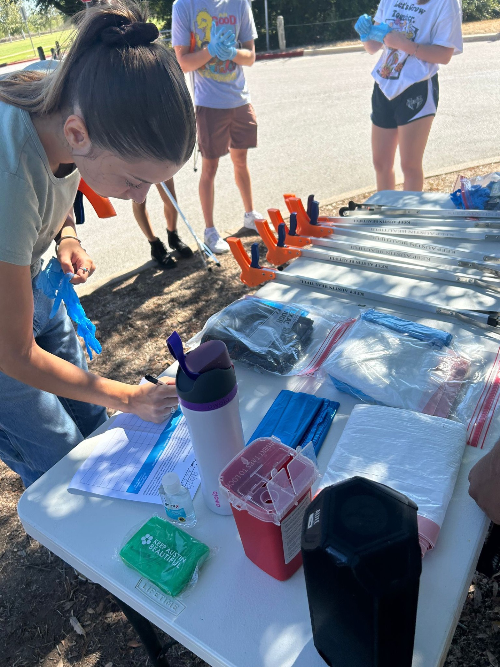 Student signing in at a Sustainability Club tabling event with cleanup supplies on the table
